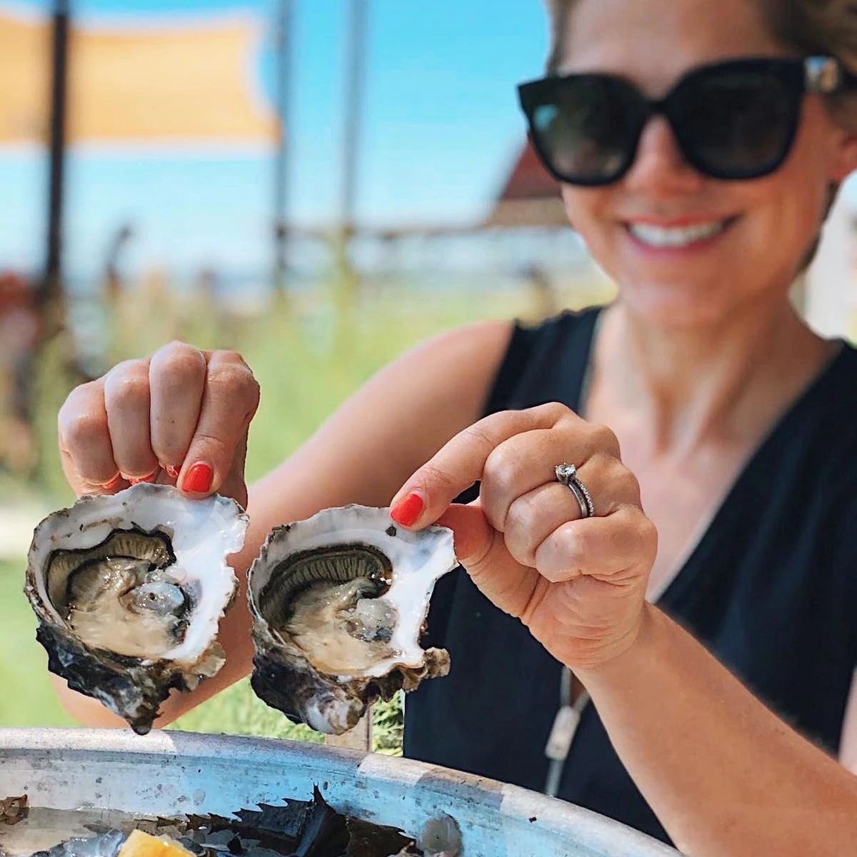Woman wearing sunglasses holds two open oysters over ice