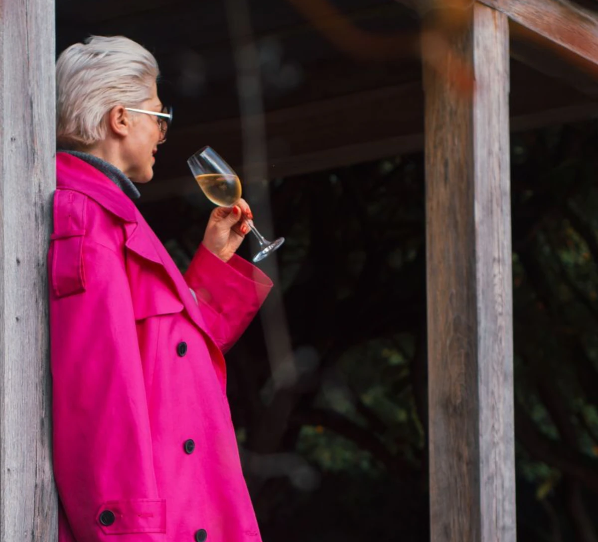 Person in bright pink coat holding a glass of white wine beside a wooden doorway