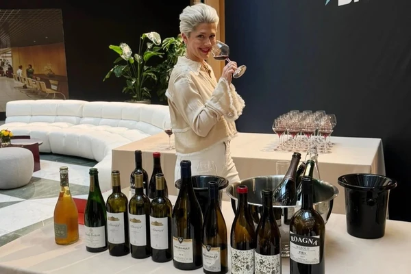Woman holding a wine glass behind a table of wine bottles and filled glasses