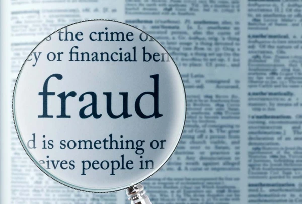Magnifying glass enlarging the word fraud in a blurred dictionary entry