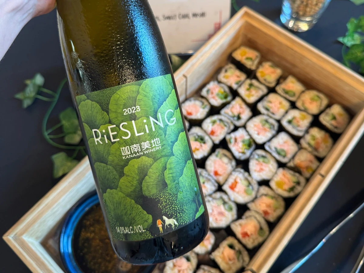 Bottle of 2023 Riesling wine held above a box of sushi rolls