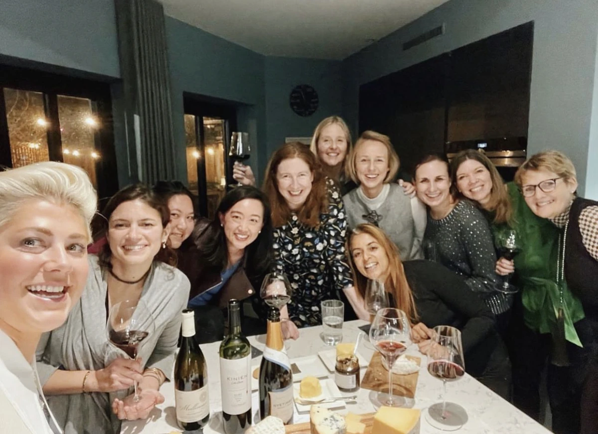 Group of women smiling around a table with wine bottles and glasses