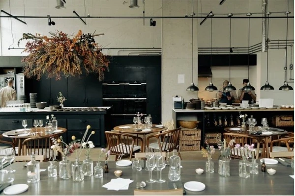 Restaurant interior with tables set for dining, hanging lights, floral arrangements and staff at the bar