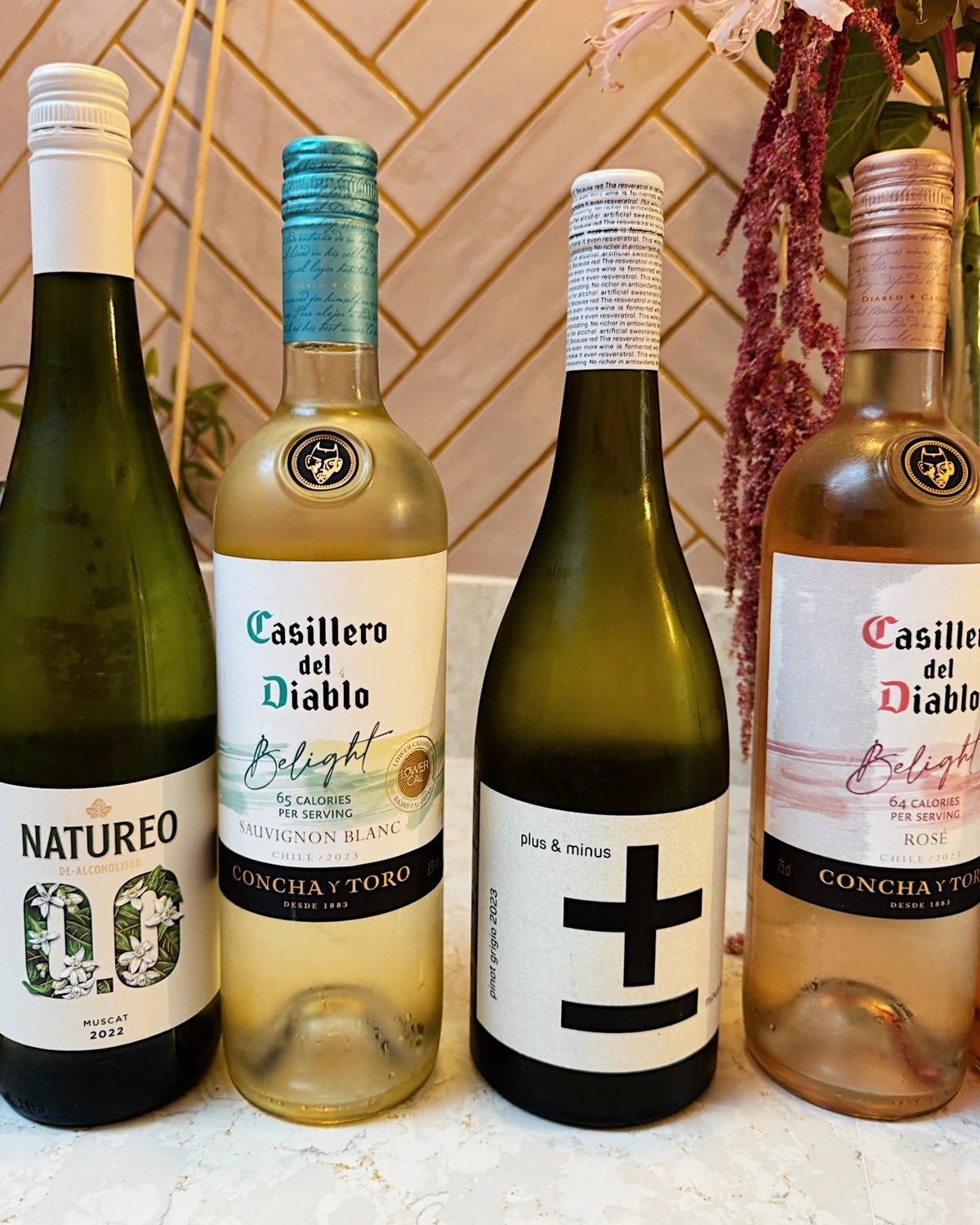 Four wine bottles displayed against a tiled wall with hanging flowers