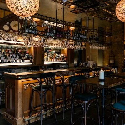 Dimly lit bar with hanging glassware, bottles, stools and tables