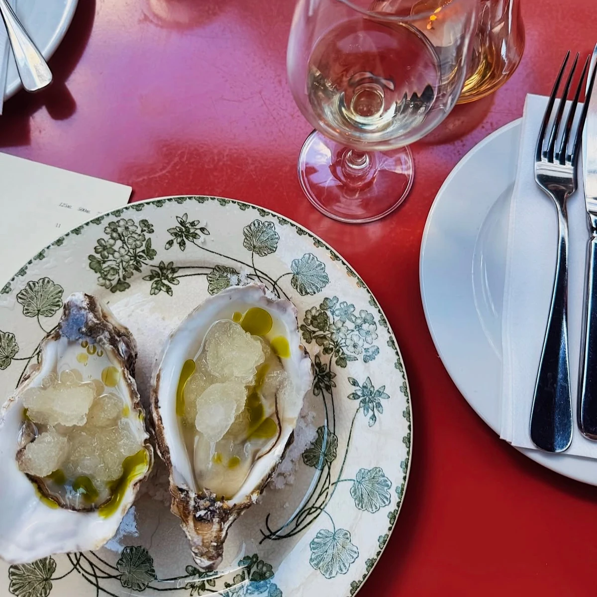 Oysters on a floral plate beside wine glasses, white plates and cutlery