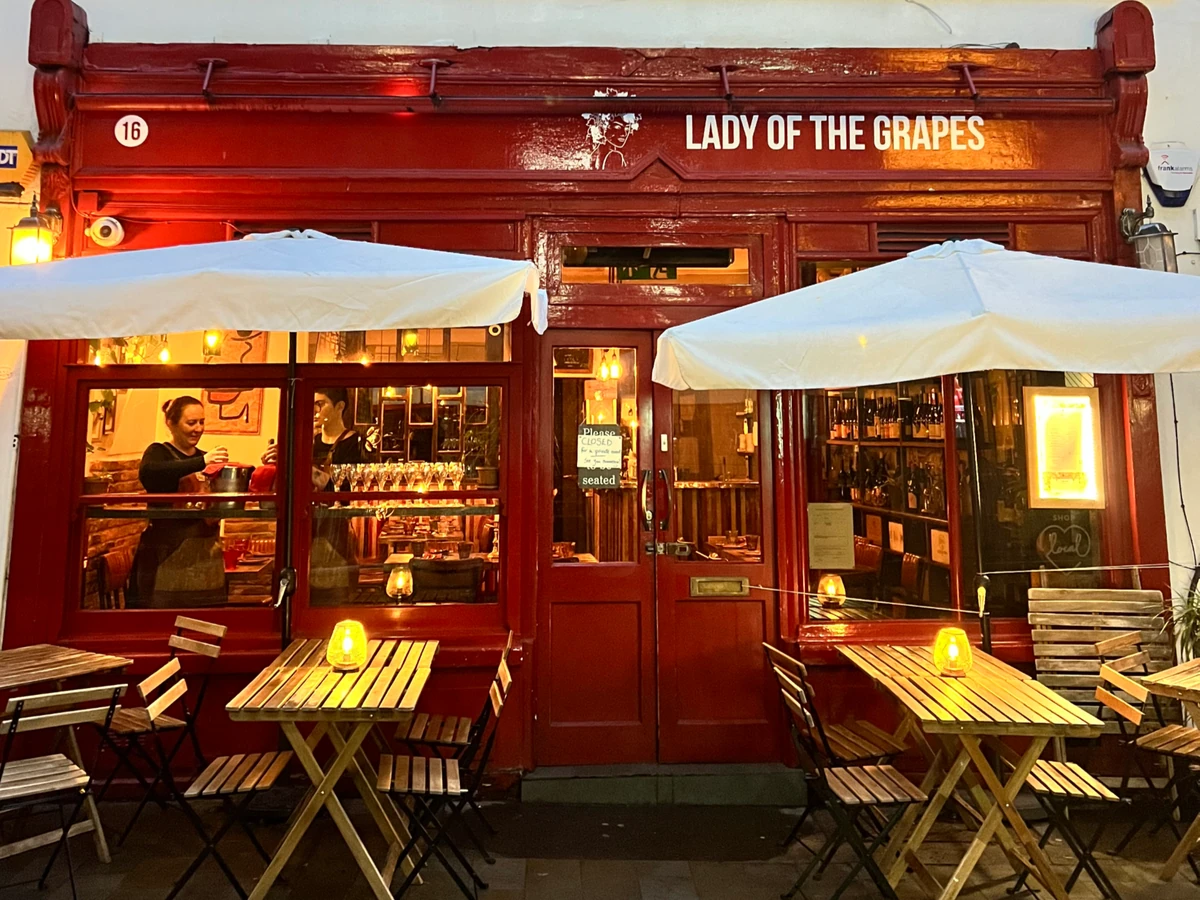 Red wine bar frontage labelled Lady of the Grapes, with outdoor tables and umbrellas