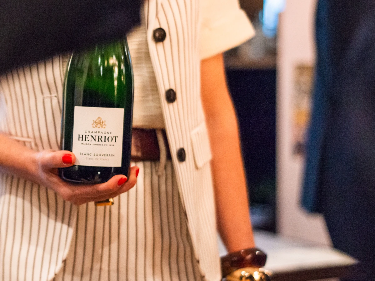 Person holding a bottle labelled Champagne Henriot Blanc de Blancs