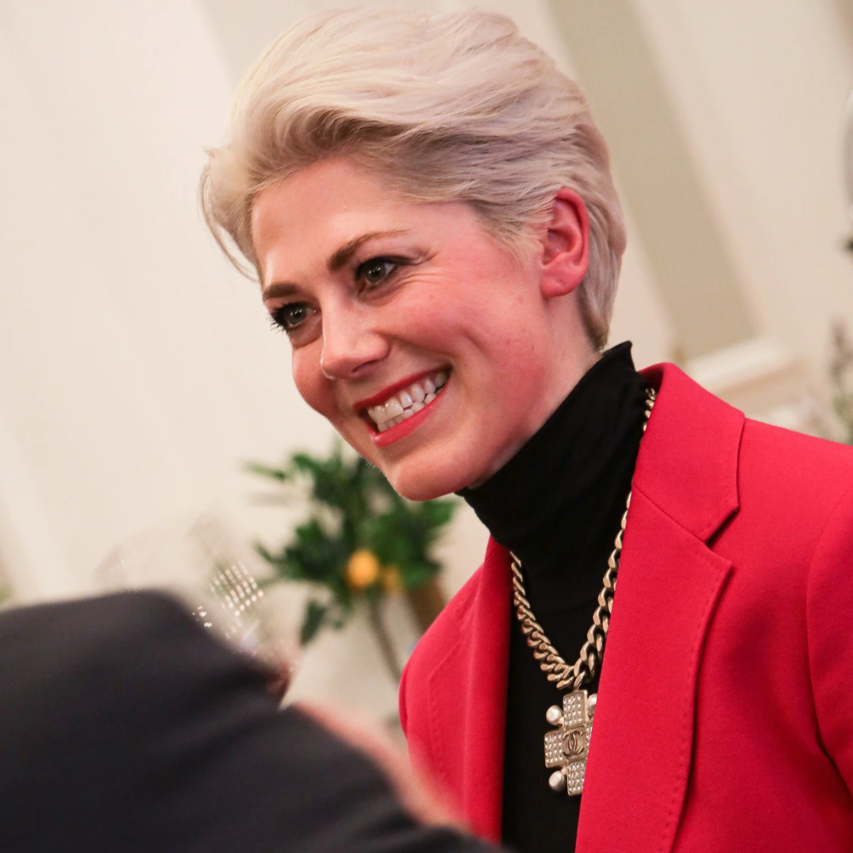 Smiling woman with short blonde hair wearing a red jacket and black top
