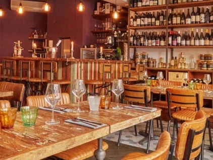 Warmly lit wine bar with bottles on shelves, tables set with glasses and chairs