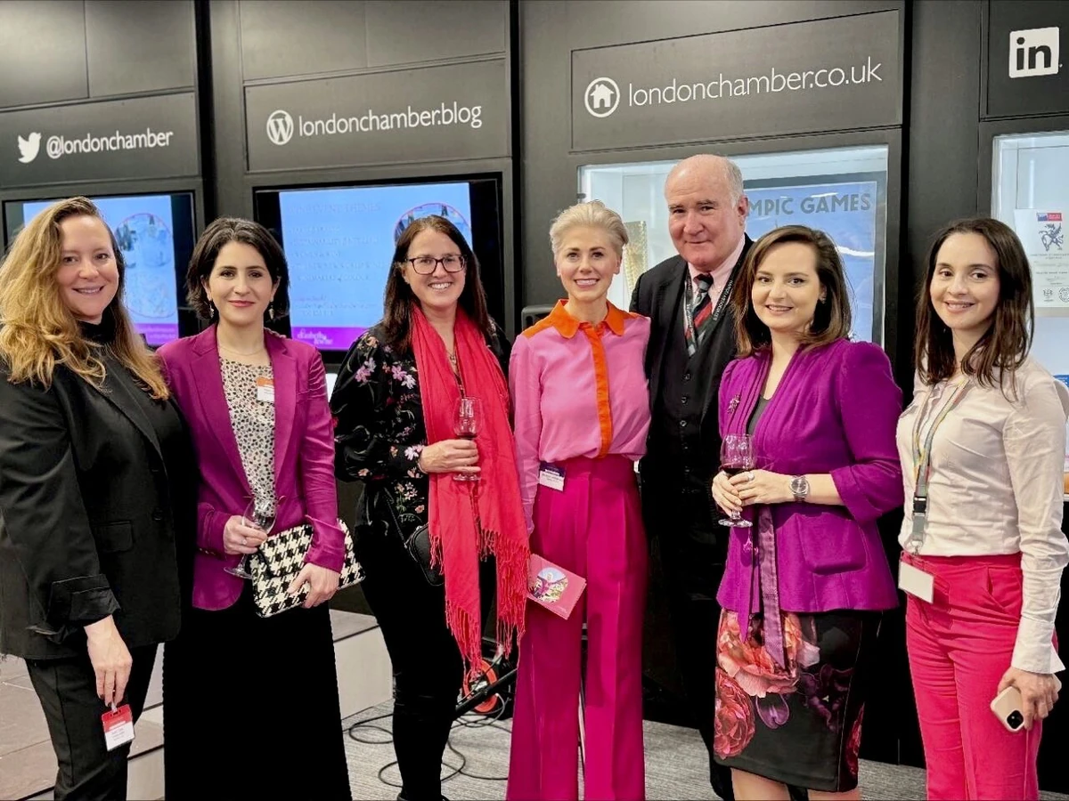 Seven people posing at a wine event, with drinks, event signage and social media logos behind them