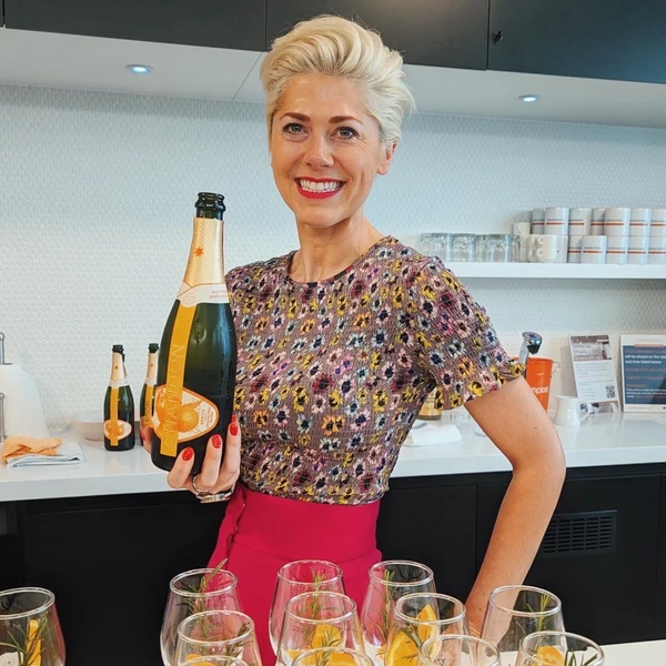 Smiling woman holding a bottle of sparkling wine behind a bar with cocktail glasses