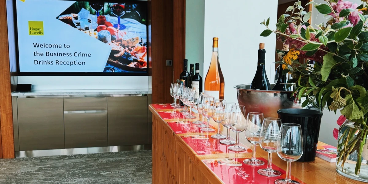 Wine reception with glasses, bottles, flowers and screen reading Welcome to the Business Crime Drinks Reception