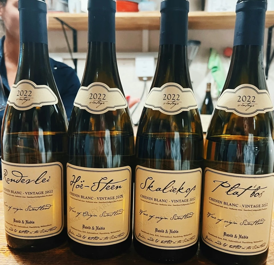 Four 2022 Chenin Blanc wine bottles from David & Nadia arranged on a wooden table