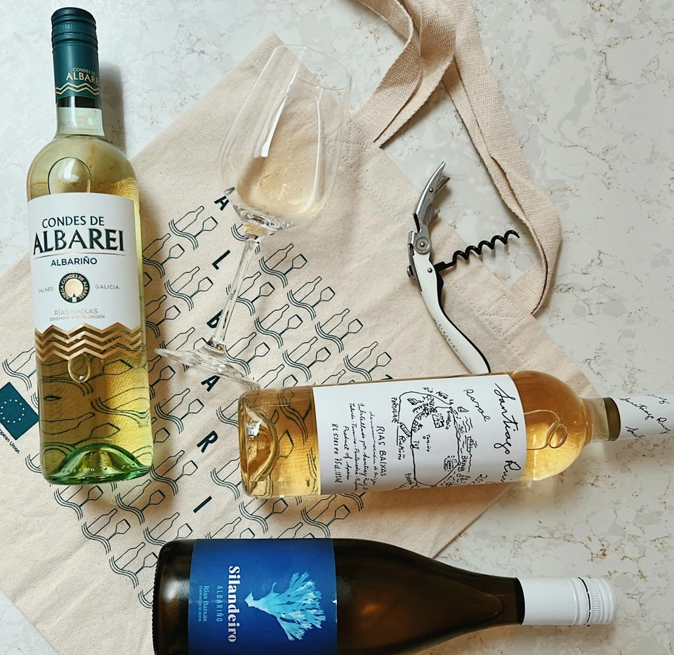 Three Albariño wine bottles, a tasting glass and corkscrew on a patterned cloth