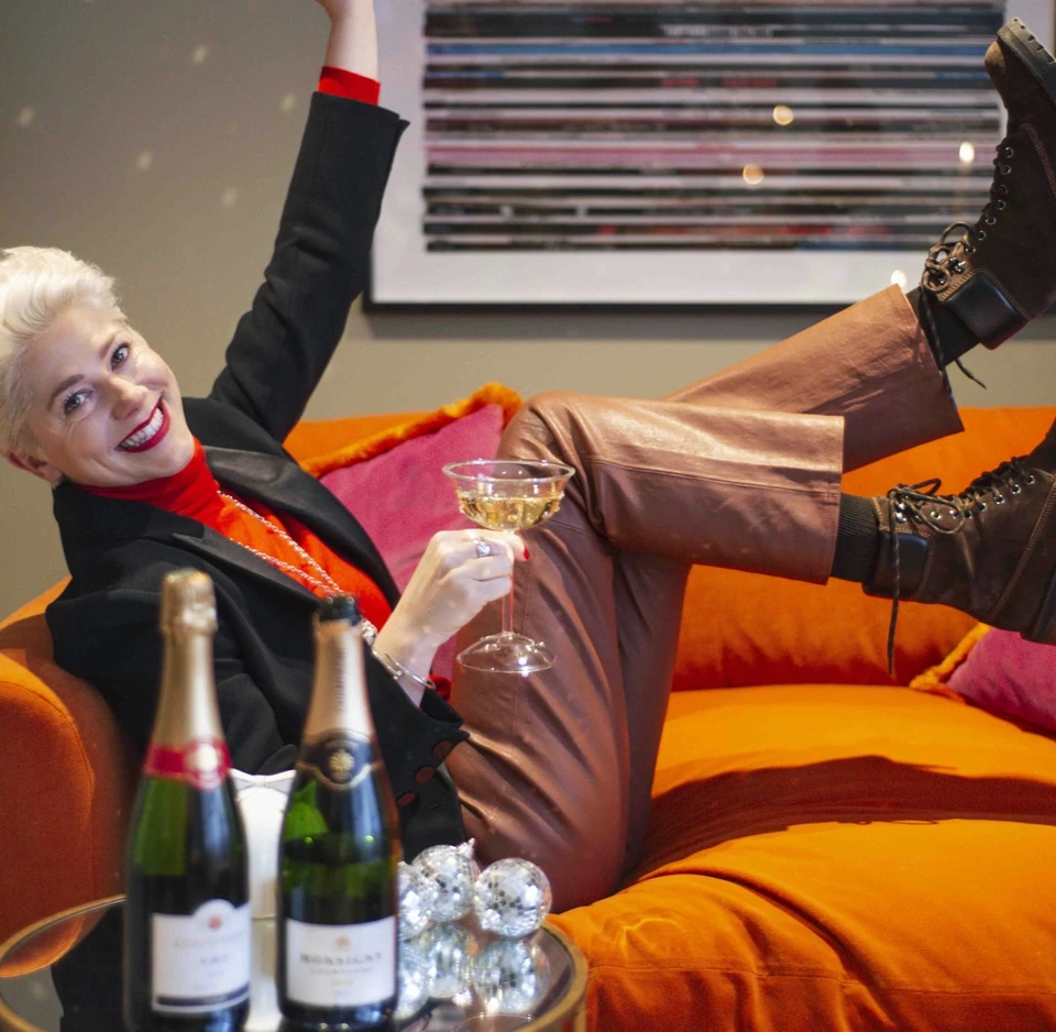 Person relaxing on an orange sofa with sparkling wine, a disco ball and raised legs