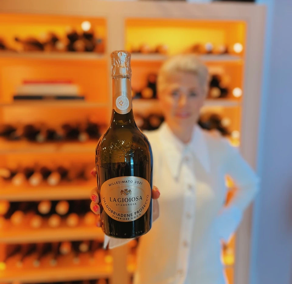 Bottle of Lagiosa Prosecco held in front of illuminated wine shelves