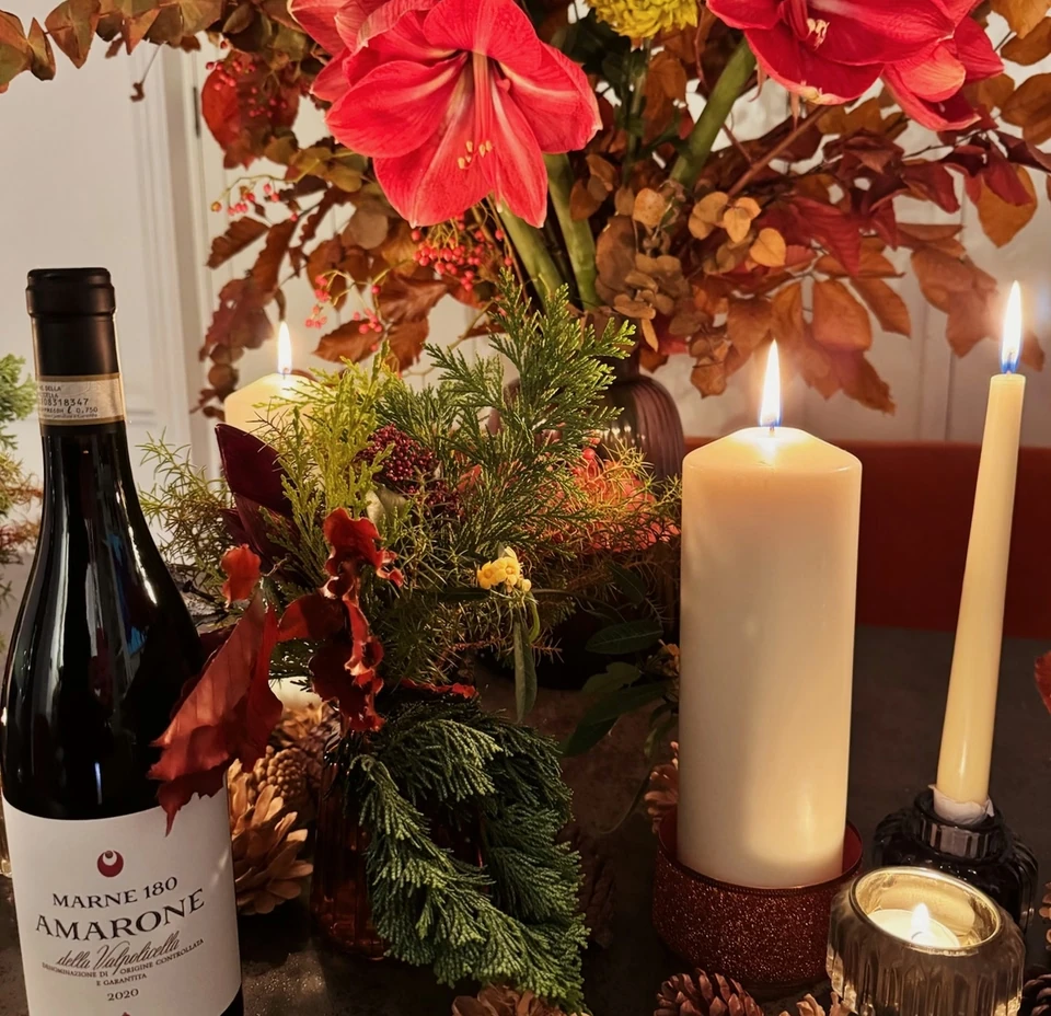 Tedeschi Amarone bottle beside autumn flowers, greenery, pine cones and lit candles