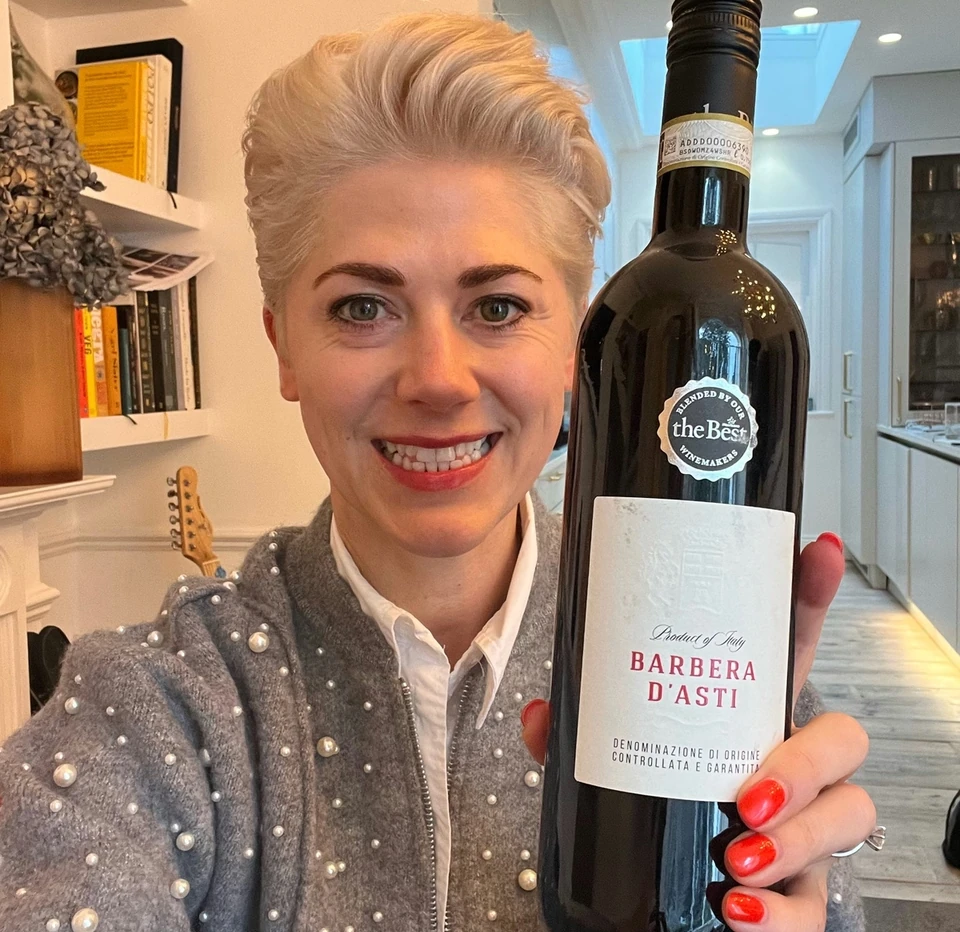 A woman holds a bottle of Barbera d'Asti wine indoors