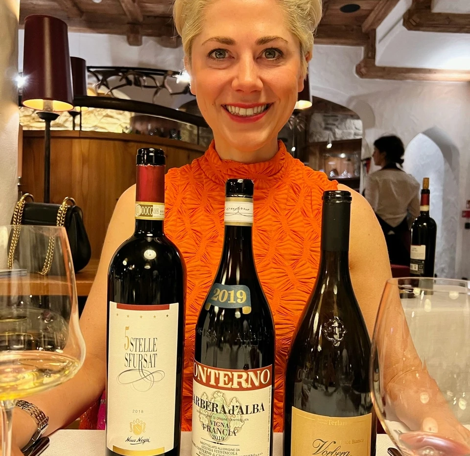 Woman presenting three Italian wine bottles, including a Barbera d’Alba