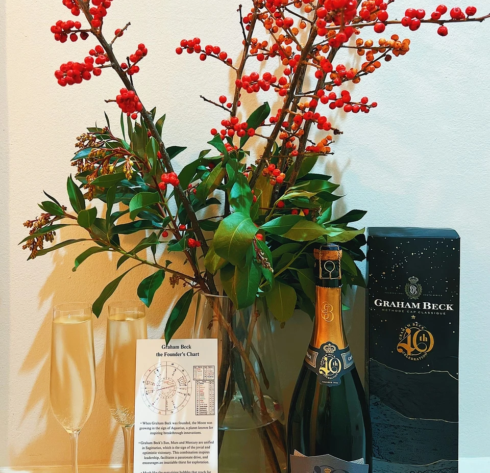 Graham Beck 40th anniversary sparkling wine bottle and box beside two flutes and a berry arrangement