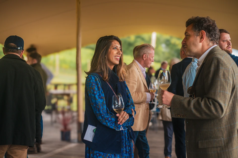 Guests mingle beneath a marquee, holding glasses of wine at an outdoor tasting