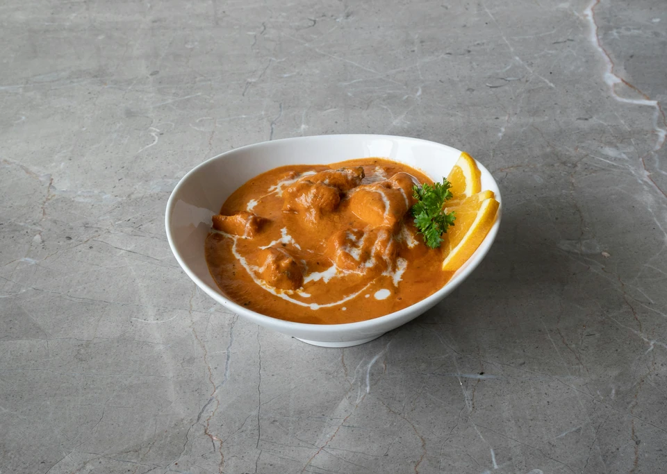 Bowl of creamy orange curry garnished with parsley and orange wedges