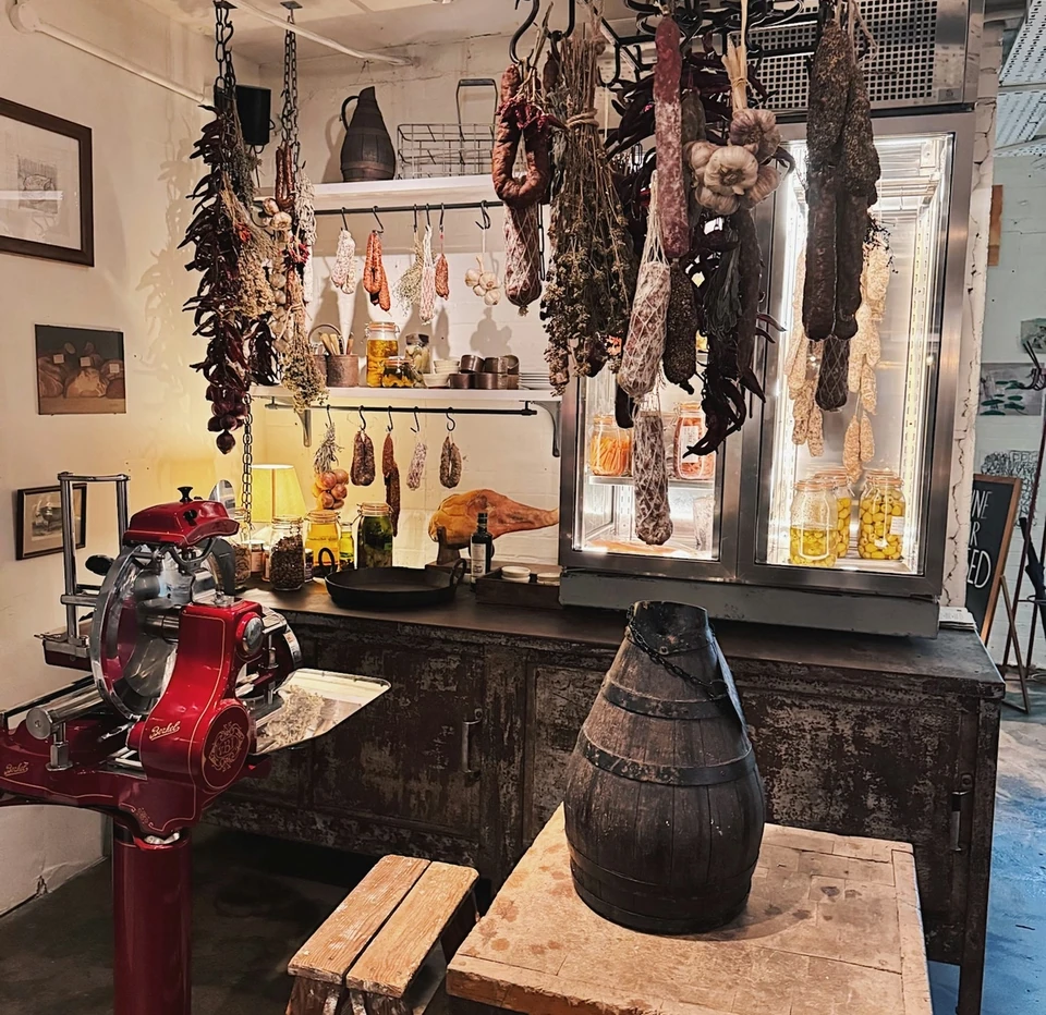 Traditional farm shop interior with hanging cured meats, preserves, a red slicer and a wooden barrel