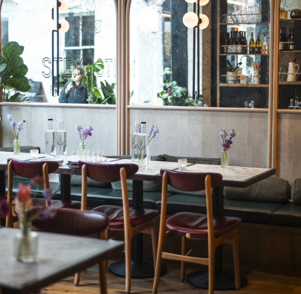 Stem + Stem restaurant interior with arched mirrors, wine bottles, flowers and set dining tables