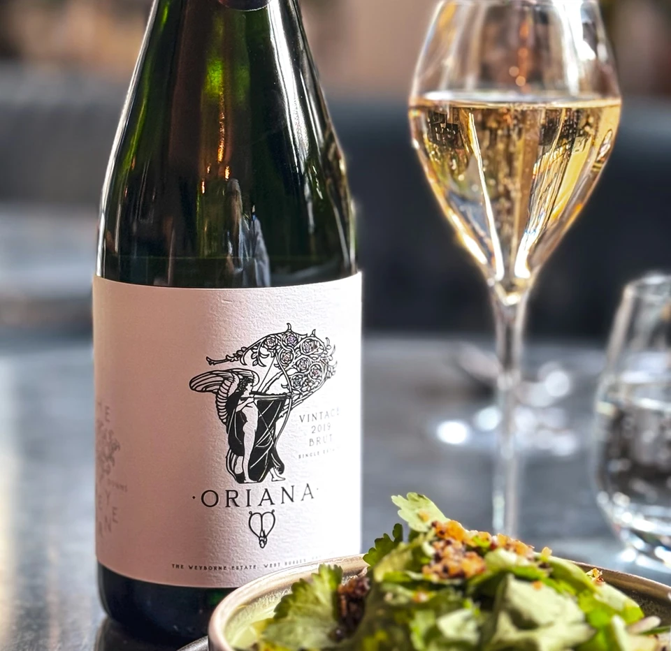Weyborne Oriana sparkling wine beside a glass and a bowl of food