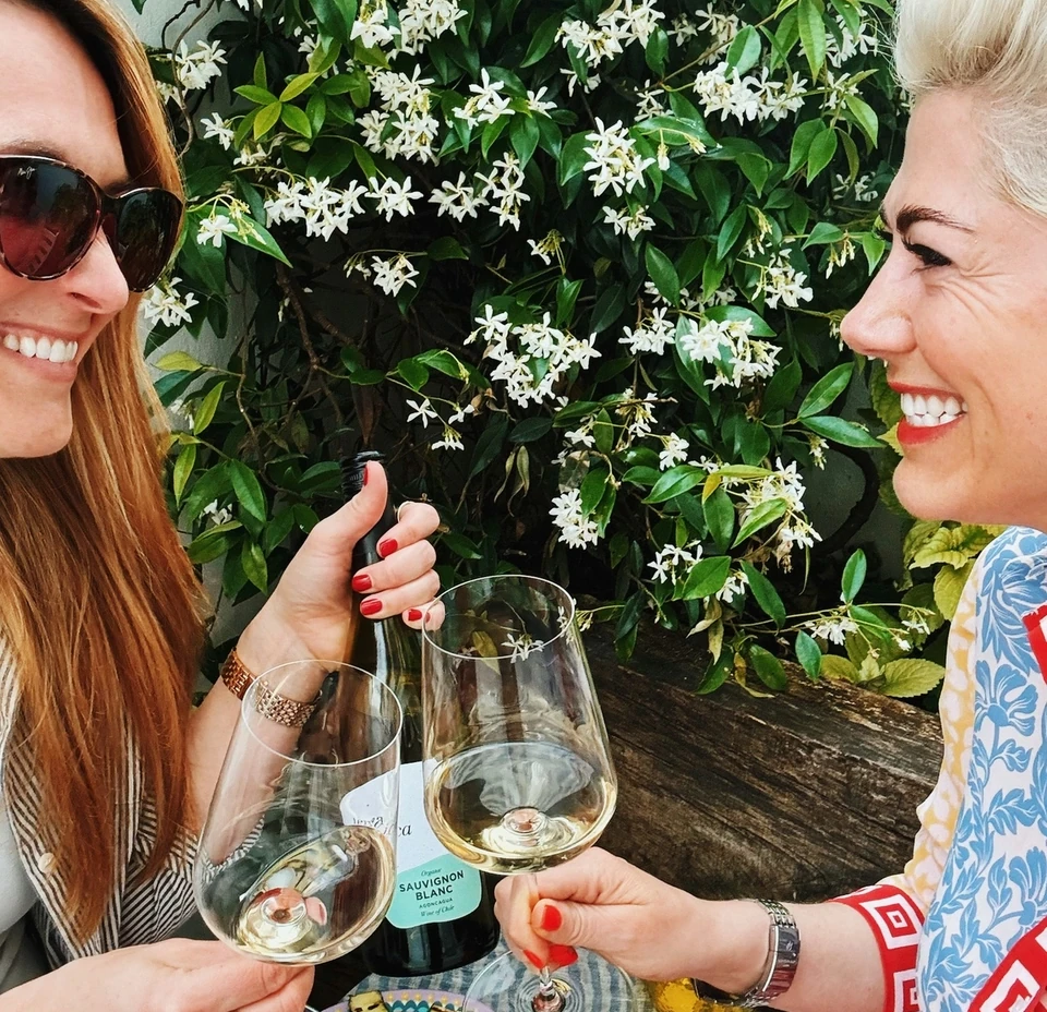 Two women raise glasses of Sauvignon Blanc beside flowering jasmine