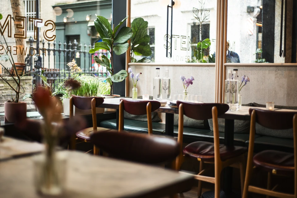Dining room at Stem + Stem with wine glasses, botanical displays and tables beside large windows