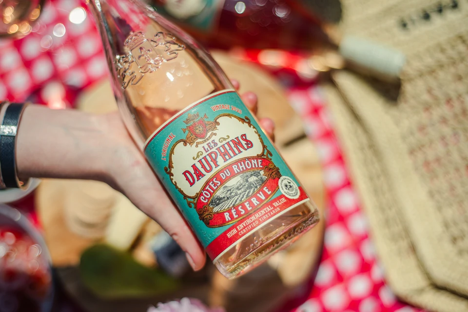 Bottle of Les Dauphins Côtes du Rhône rosé held over a wine tasting table