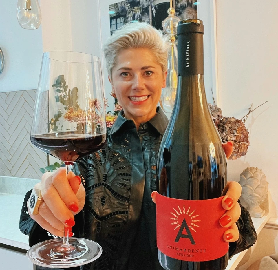 Woman holding a glass of red wine and an Animardente Etna DOC bottle indoors