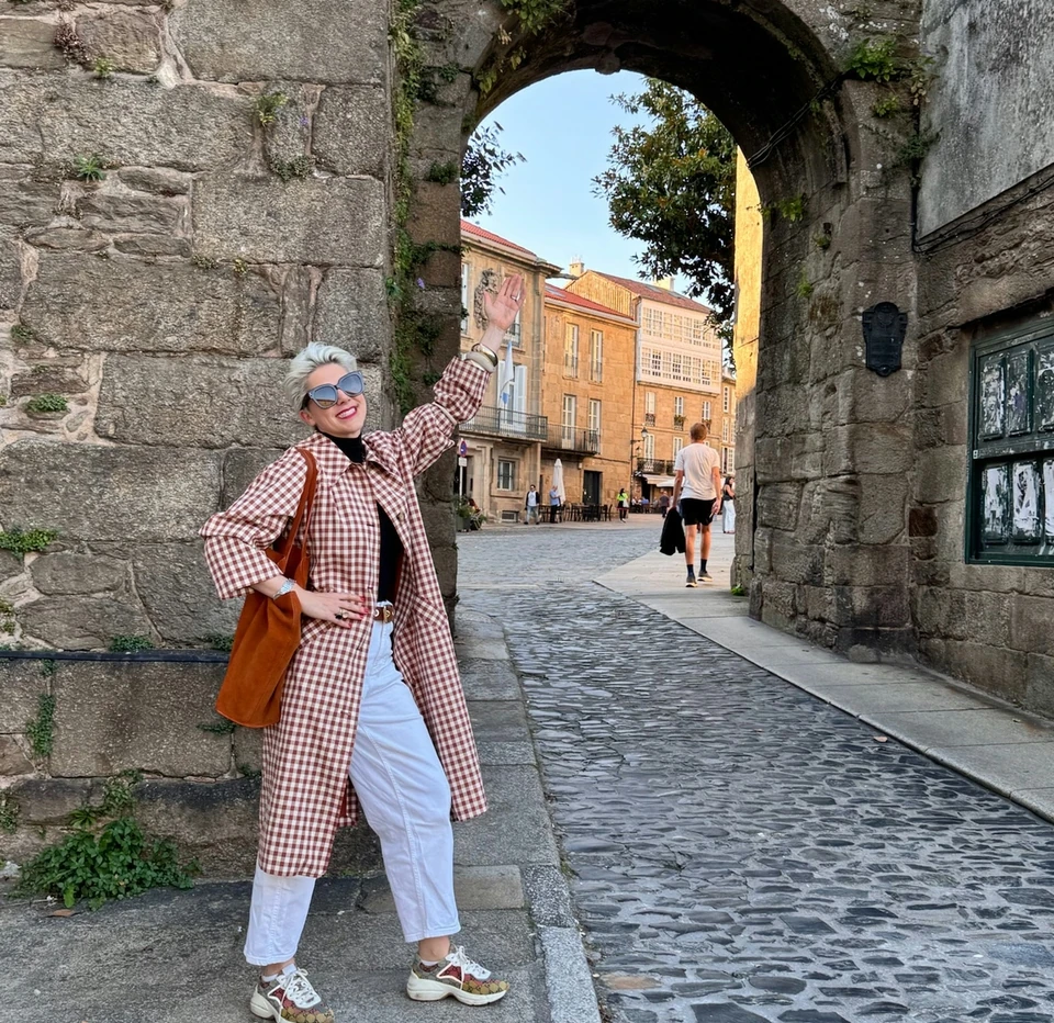 Woman posing beneath a historic stone arch on a cobbled street