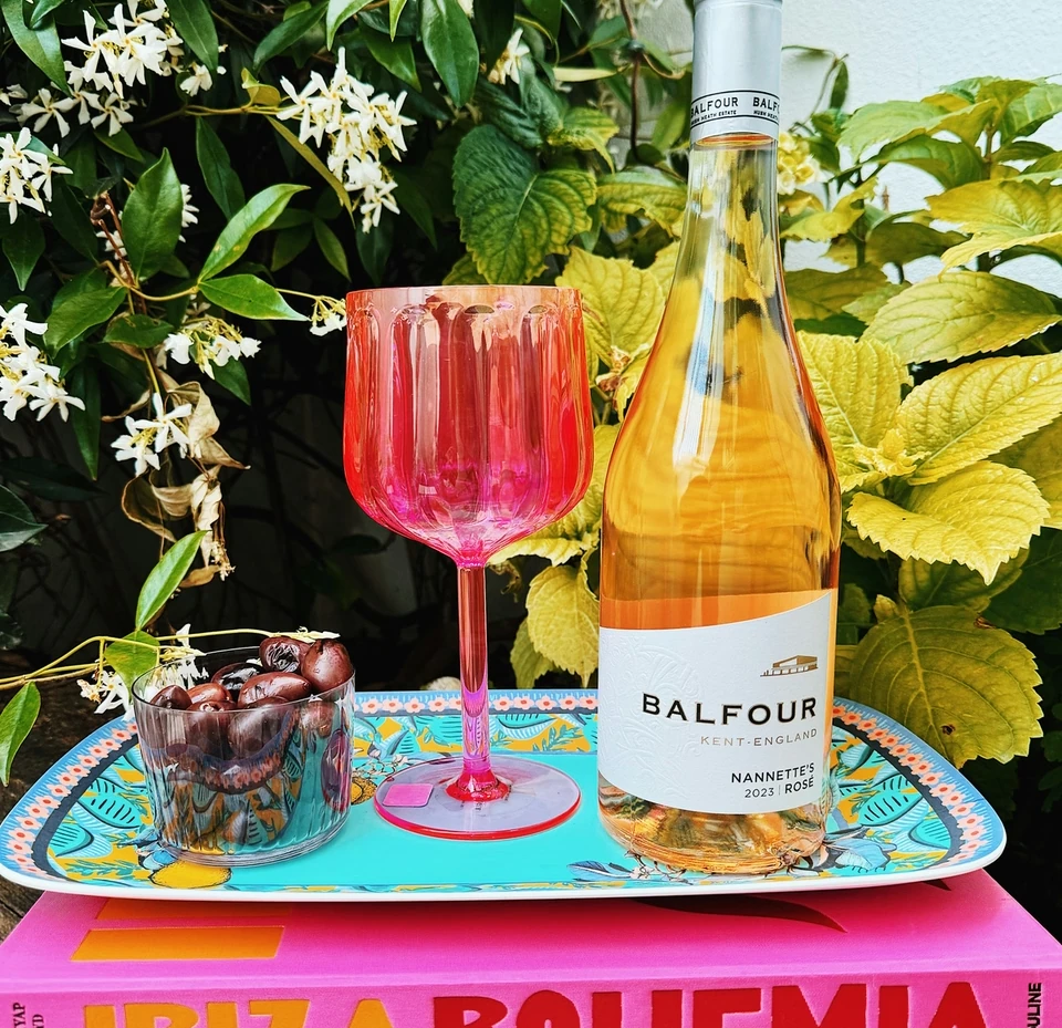 Balfour rosé wine bottle and pink wine glass on a colourful tray beside cherries and flowers