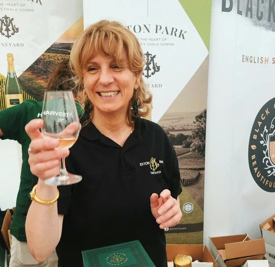 A woman holding a glass of English sparkling wine at an Exton Park Vineyard display.