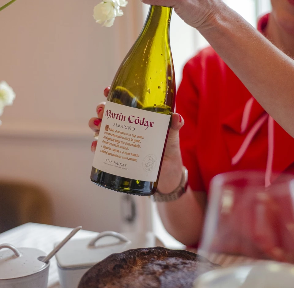 Person holding a bottle of Martín Códax Albariño beside flowers and bread