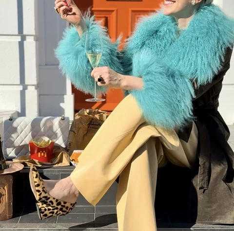Person in a turquoise coat holding sparkling wine and fried chicken outside an orange door