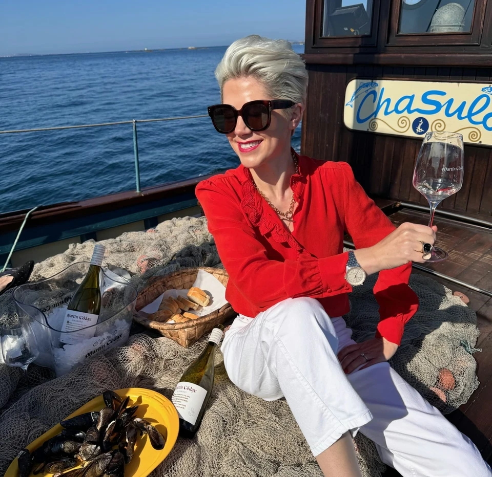 Woman in a red blouse holding a wine glass on a boat beside mussels, bread and wine bottles