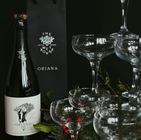 The Weyborne Oriana sparkling wine bottle beside coupe glasses and festive greenery