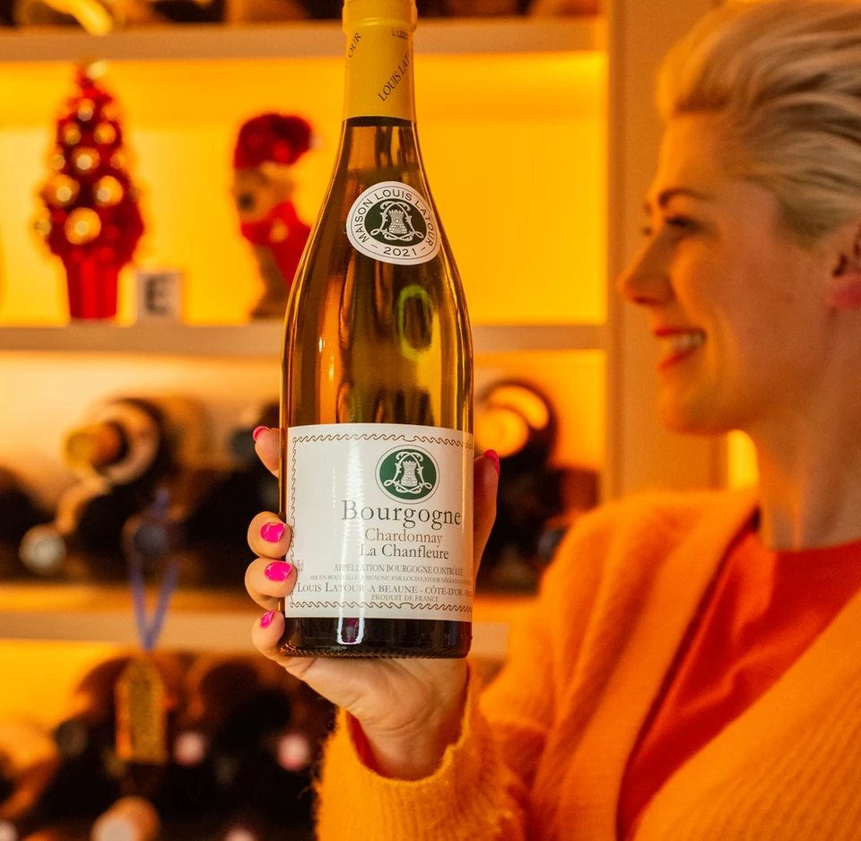 Bourgogne Chardonnay bottle held in front of wine displays by a person in an orange jumper
