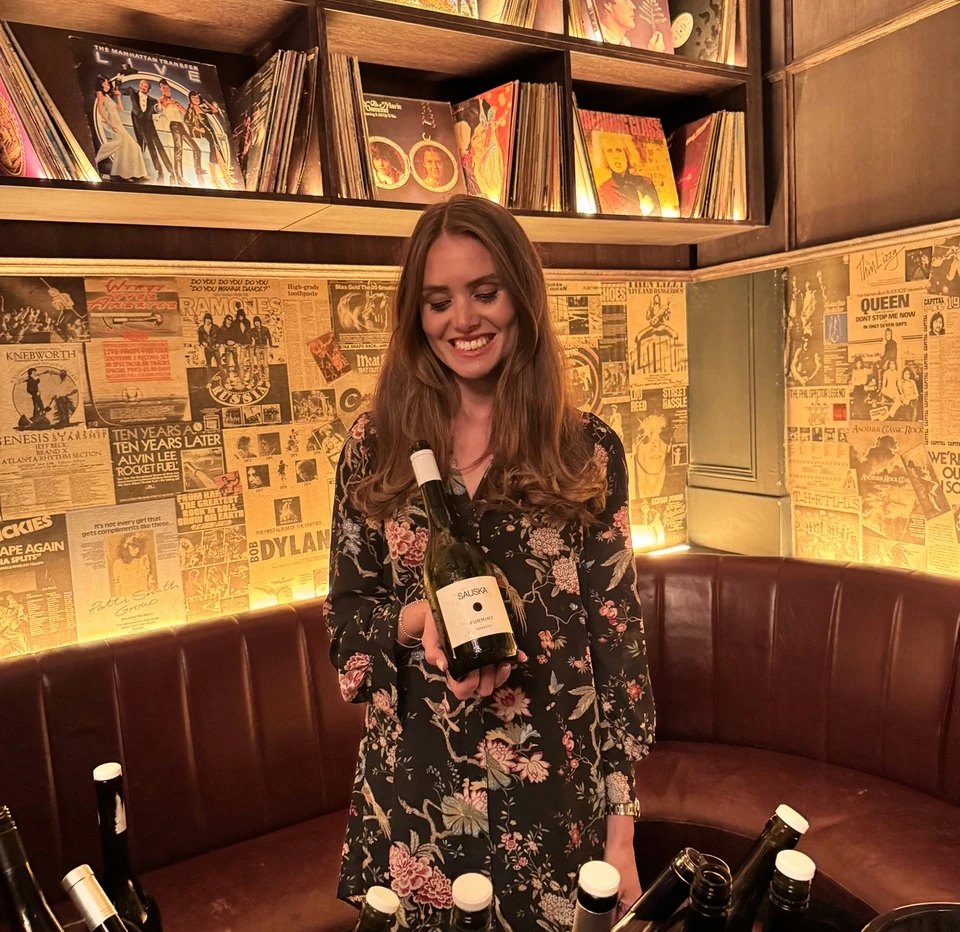 Woman holding a Sauska Furmint bottle in a music-themed bar