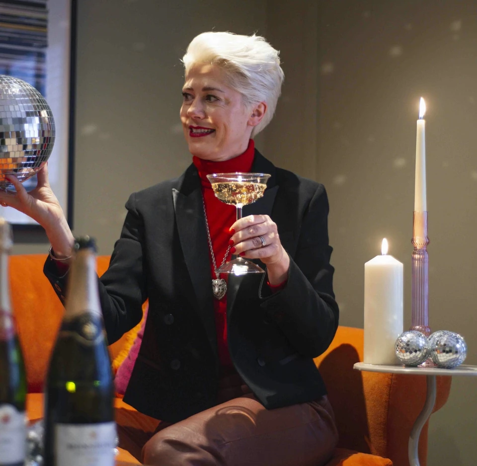 Woman in a black jacket holds a glass of sparkling wine beside candles and disco balls