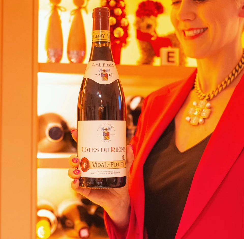 A woman in a red jacket holds a bottle of Vidal-Fleury Côtes du Rhône
