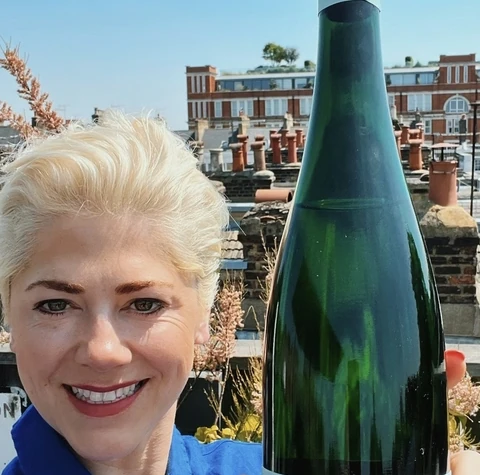 A woman holds an Ansgar Clüsserath Steinreich Riesling 2020 bottle on a sunny rooftop
