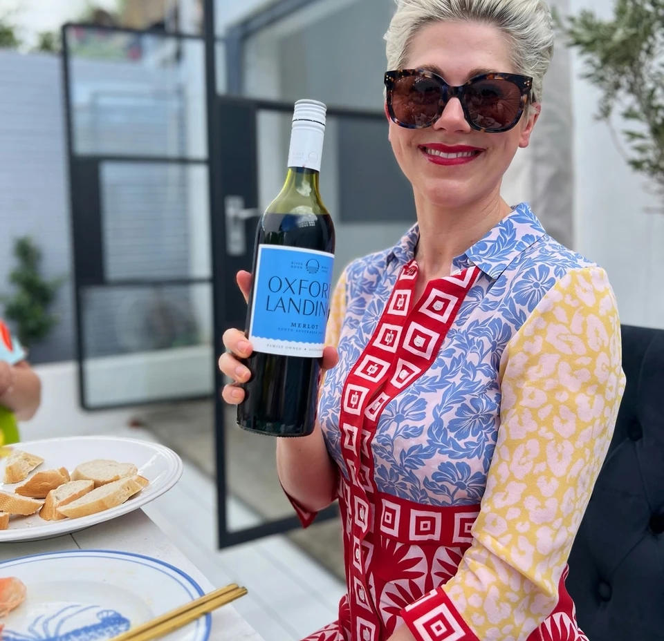 Guest holding an Oxford Landing Merlot bottle at a dining table