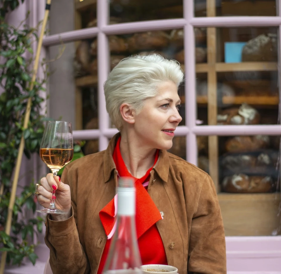 Woman holding a glass of Bolney rosé beside a pastry and coffee in a café