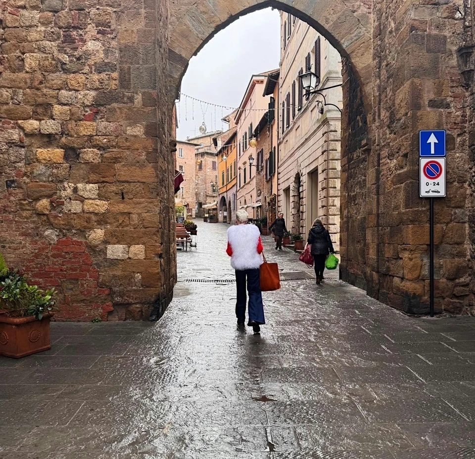 Rainy historic street viewed through a stone archway in Montalcino, Tuscany