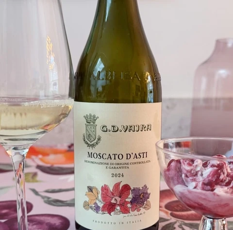 Moscato d’Asti bottle beside a filled wine glass, pink dessert and silver jug